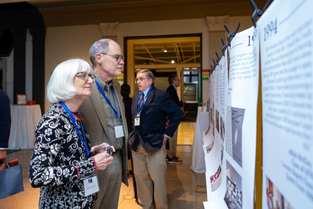 People with badges view a series of informational posters on display at an indoor event.
