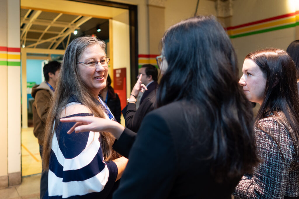 People engaged in conversation at an indoor event, standing in groups near a doorway.