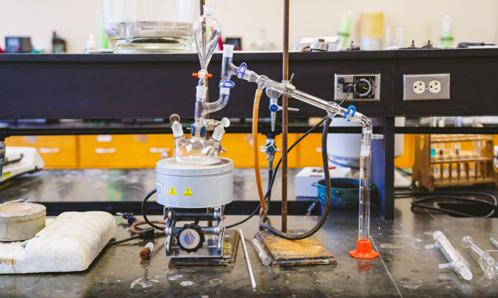 A laboratory setup with glassware and a heating mantle for chemical distillation on a black countertop.